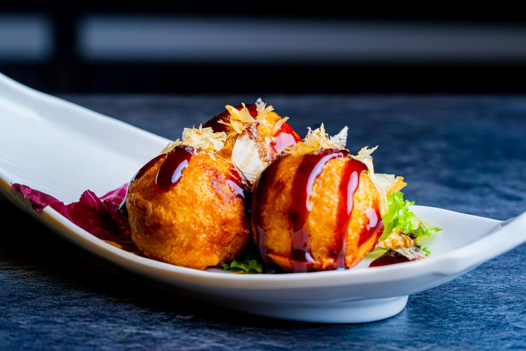 Une assiette élégante de trois boules de Takoyaki au poulpes avec une sauce rouge par dessus