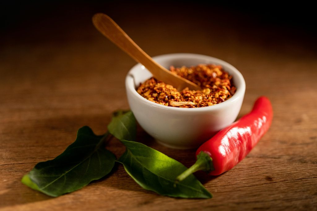 Petit bol de piment rouge écrasé avec un piment rouge et une feuille verte à côté 
