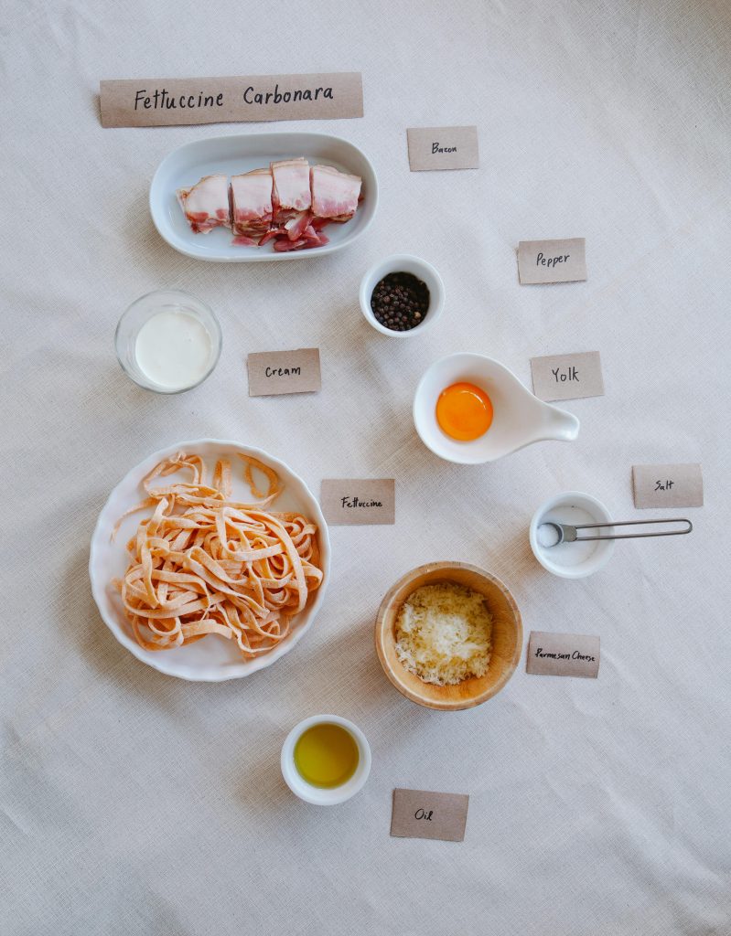 ngrédients pour des pâtes carbonara traditionnelles : spaghetti, œufs, pancetta, parmesan râpé, poivre noir et sel, disposés sur un plan de travail.